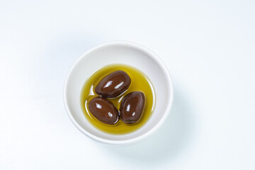 Black olives in a small casserole with olive oil on a white surface background