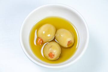Green olives in a small casserole with olive oil on a white surface background