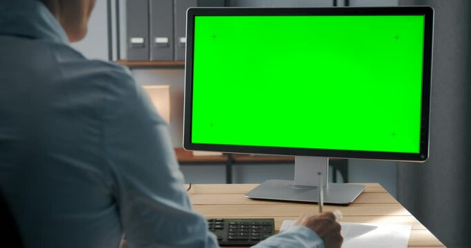 View from shoulder of female worker in blue shirt having video chat with colleagues on computer with chroma key screen. Mature woman solving working issues on distance.