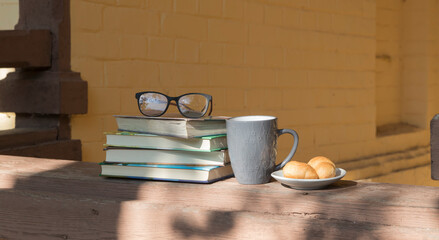 A cup, books and a plate of croissants on the veranda in the shade of the trees. Cozy place to read and relax