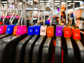 Different sized hanger with colourful dress size tags XL L M XS t shirts displayed in shop for sale