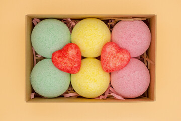 Isolated photo of a box with bath bombs in different colors and sizes on a peach background