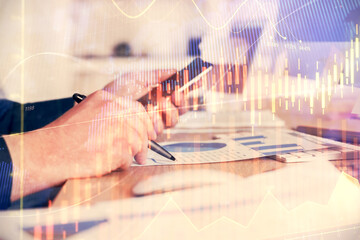 Double exposure of man's hands holding and using a phone and financial graph drawing. Analysis concept.