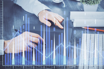 Double exposure of man's hands holding and using a phone and financial graph drawing. Analysis concept.