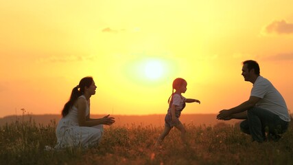 little daughter goes from mom to dad, hugs and kisses her parents in rays of warm sun. Happy family walks in park at sunset. Mom, dad and baby. healthy family plays in field. Happy family concept