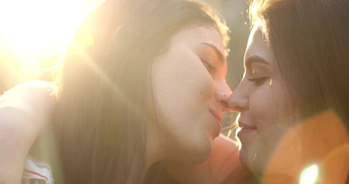 Young women in romantic moment between two gay lesbian girlfriends outside with lens-flare