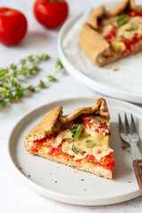 Slice of galette with tomatoes and cheese. Whole wheat rustic pie with tomatoes, cheeseand herbs. Healthy food concept.