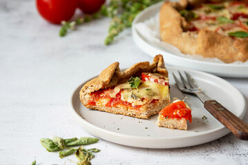 Slice of galette with tomatoes and cheese. Whole wheat rustic pie with tomatoes, cheeseand herbs. Healthy food concept.