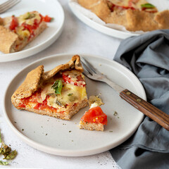 Slice of galette with tomatoes and cheese. Whole wheat rustic pie with tomatoes, cheeseand herbs. Square image.