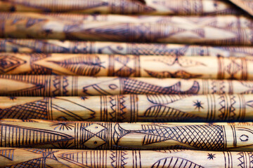 hand made wooden bamboo carving engraved fish figure artwork on bamboo, rows of engraved bamboo sticks. textured background. tribal artwork.