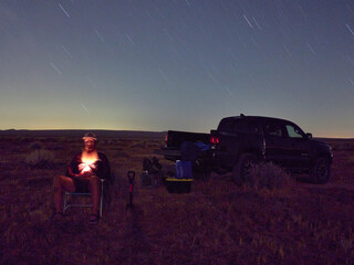 Man sits in chair in the dark, in the desert, flashlight on face.