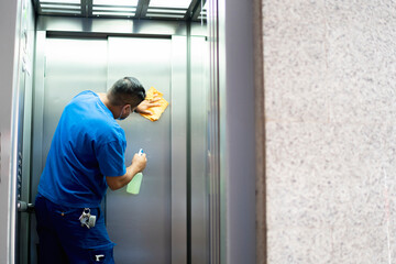 maintenance personnel disinfecting the elevator walls to avoid covid19 - obrazy, fototapety, plakaty