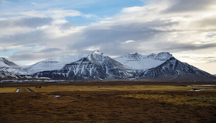 Snow covered peaks in an Icelandic landscape with orange grass and clouds