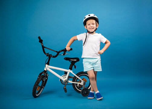 A child toddler with a child's bike and in a protective helmet stands on a blue background and looks into the camera. Studio photo for articles on safety and kid sports and activity.