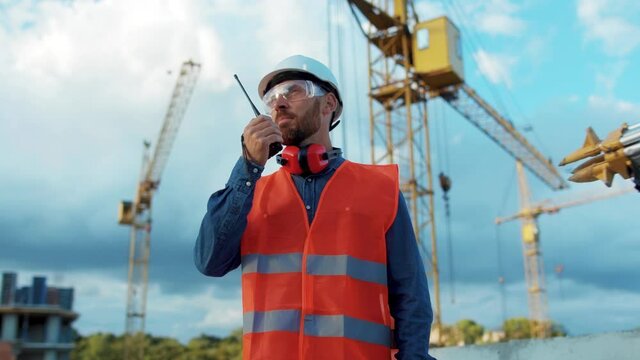 Man builder engineer worker in hard hat with use a walkie-talkie on construction helmet industrial site industry structure architecture inspector builder slow motion