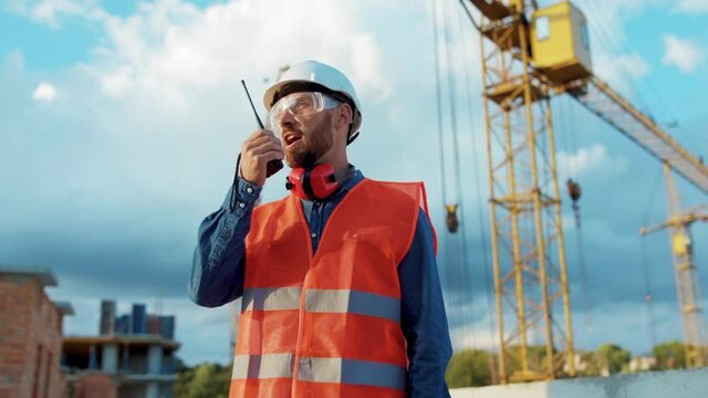 Serious man builder engineer worker in hard hat with use a walkie-talkie on construction helmet industrial site industry structure architecture inspector builder slow motion