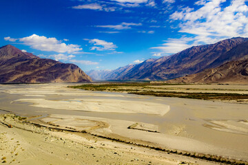 Fototapeta na wymiar High dynamic range image of barren mountain in a desert with river and deep blue sky and white patchy clouds in ladakh, Jammu and Kashmir, India