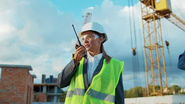 Woman builder engineer worker in hard hat with use a walkie-talkie on construction helmet industrial site industry structure architecture inspector builder slow motion