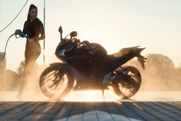 Beautiful pretty girl washes a motorcycle at self-service car wash in the city at sunrise. Taking care about vehicle. © gorynvd