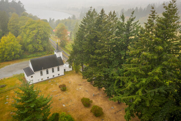 Aerial View of a Little White Church on a Foggy Morning. Atmospheric look at  a Congregational Church and the graveyard accompanying the building. The Salish Sea can be seen in the background.