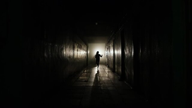 General plan of the chase. A silhouette of a girl runs out of the light at the end of the hallway and runs straight towards the camera. She is being chased by a limping stalker with an ax