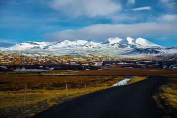 Road leading to a mountain range with white capped peaks in an Icelandic landscape