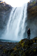 Obraz premium Woman standing in front of a powerful waterfall with mist and wind in Iceland