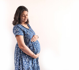 A pregnant indian lady with blue dress and hands on belly.