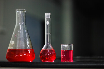 red liquid in a round bottomed flask and glass beaker and conical flask on a black granite table in...
