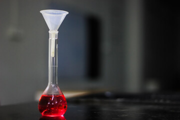 red liquid in a round bottomed flask with funnel on a black granite table in dark background