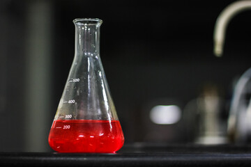 red liquid in a glass conical flask on a black granite table in dark background