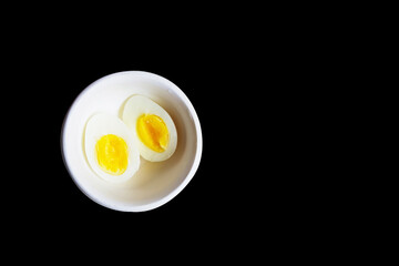 boiled egg cut in half in a white bowl in black background with space for text