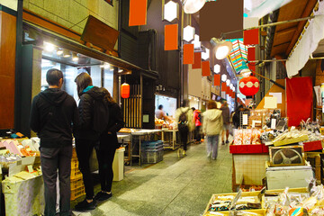京都市の中心地にある錦市場内の店舗の景観。錦市場は、真ん中の小道の両側に食材の商店が並んだ３９０ｍの商店街。近年は外国人観光客を中心に賑わっている。
