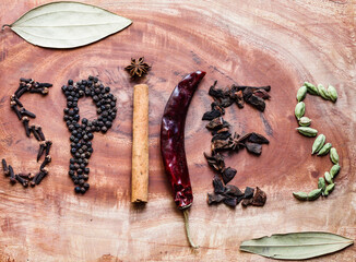 Typical ingredients for a garam masala black peppercorns, mace, cinnamon, cloves, dried red chilli and green cardamom in a wooden background