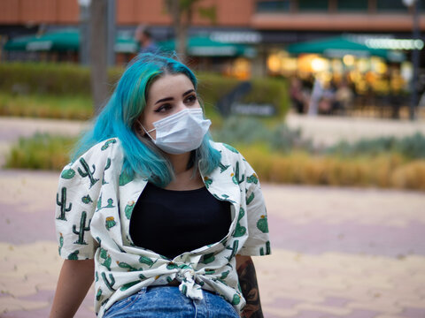 Mujer joven con los pelos de colores y tatuajes vistiendo mascarilla durante la pandemia del coronavirus respetando las medidas de seguridad y distanciamiento social del covid-19