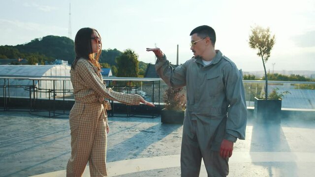 Street dance. Hip hop culture. Competitive young active man and woman gesturing doing high-five dancing in front of each other on rooftop. Dance battle. Break dance. Modern youth.