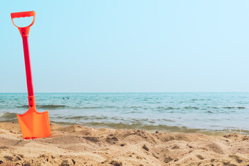 Fototapeta na wymiar Kid's toy orange shovel stuck in a sand at the beach sea shore