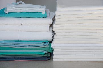 Stack of folded white linens and green surgery clothes in an industrial laundry.