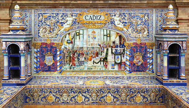 Image with the name of the spanish city of Cadiz and a historical scene painted on ceramic tiles - seating benches in Spain Square in Seville