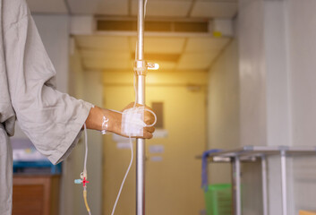 Hands patient man with intravenous saline on stainless pole during walking at the hospital