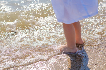 Small baby feet close-up on the sand of the sea beach. Sea water washes the feet. Happy childhood. Rest at the sea. Summer sunny day. Copy space.