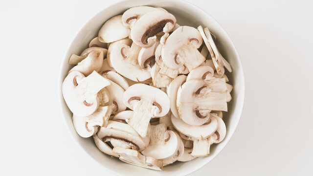 Bowl of fresh row chopped mushrooms close up on whiite background, flat lay