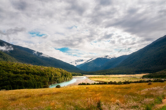 A patch of sunlight at Cameron Flat's picturesque landscape in Mount Aspiring National Park along Makarora River, with snow-capped mountain peaks engulfed in clouds in New Zealand, South Island.