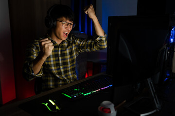 Excited asian man pro gamer sitting at the table, playing and Winning in online video games on a...