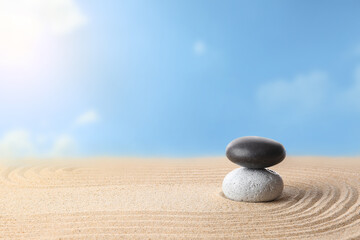 Fototapeta na wymiar Stones on sand with lines against blue sky. Zen concept