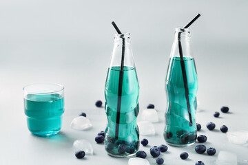 Bottles of fresh blueberry ice tea on light background