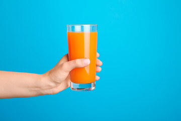 Hand with glass of fresh juice on color background