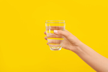 Hand with glass of water on color background