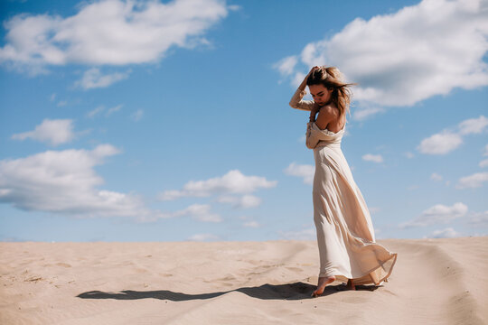 Young, slender girl in beige dress walks in the desert