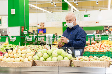 A masked man in a supermarket in the fruits and vegetables section.